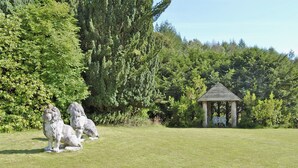 A grassy area with two stone lion statues and a wooden gazebo.