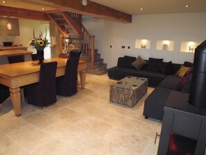 Un salon comprenant une table à manger en bois, des canapés foncés, une table basse, une cheminée et un escalier.