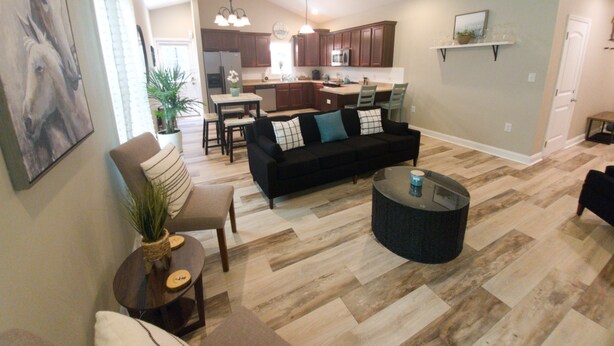 A spacious living room with a black sofa, a coffee table, and a dining area with a kitchen in the background. - Horse Ranch Getaway (Richlands)
