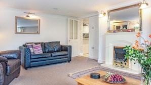 A living room with a black leather sofa, a wooden coffee table with a fruit bowl, a fireplace, and a large mirror. - Westerlands Apartment (Torquay)