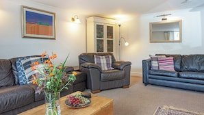 A living room with two leather sofas, a coffee table with a vase of flowers, and a rug. - Westerlands Apartment (Torquay)