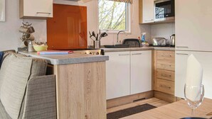 A compact kitchen with a central island, wooden cabinets, a stainless steel range hood, and a window with a view of trees. - 2 bedroom accommodation in Brocklebank, near Caldbeck and Uldale (Brocklebank, near Caldbeck and Uldale)