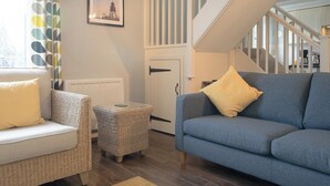 A living room with a blue sofa, a wicker chair, a small table, and a staircase. - 2 bedroom accommodation in Craster (Craster)