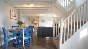 A dining area with a wooden table and blue chairs, a sofa, and a staircase with white railings. - 2 bedroom accommodation in Craster (Craster)