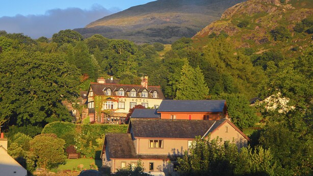 A traditional building with a sign that reads "Sun Hotel," surrounded by lush greenery and hills in the background. - 4 bedroom accommodation in Coniston (Coniston)