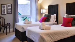 A hotel room with two beds, a window with curtains, a bedside lamp, and framed pictures on the wall. - 4 bedroom accommodation in Coniston (Coniston)