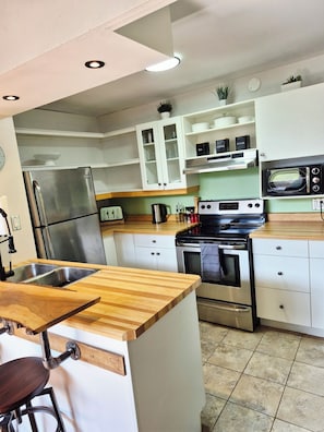 A kitchen with a stainless steel refrigerator, a microwave, an oven, and a wooden countertop.