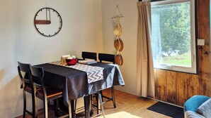 Ein Essbereich mit Holzboden, einer Uhr, einem Tisch mit Stühlen und Blick durch ein Fenster.