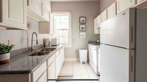 A modern kitchen with white cabinets, a granite countertop, a stainless steel sink, and a refrigerator. - Uptown Glam - Best Amenities & Neighborhood (New Orleans)