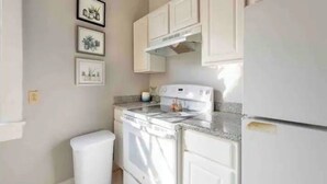 A kitchen with white cabinetry, a stove, a refrigerator, and three framed pictures on the wall. - Uptown Glam - Best Amenities & Neighborhood (New Orleans)