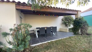 An outdoor patio with a table and chairs, surrounded by plants and a tiled floor.