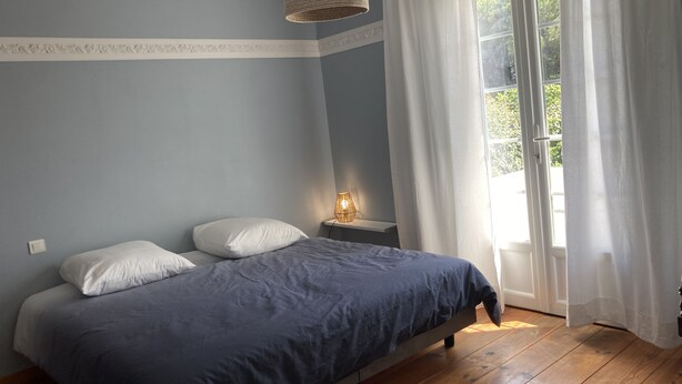 A bedroom with a bed, a bedside table with a lamp, and a window with curtains.