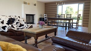 A living room with a fireplace, a dining area with a table and chairs, and a large window with a view of greenery.