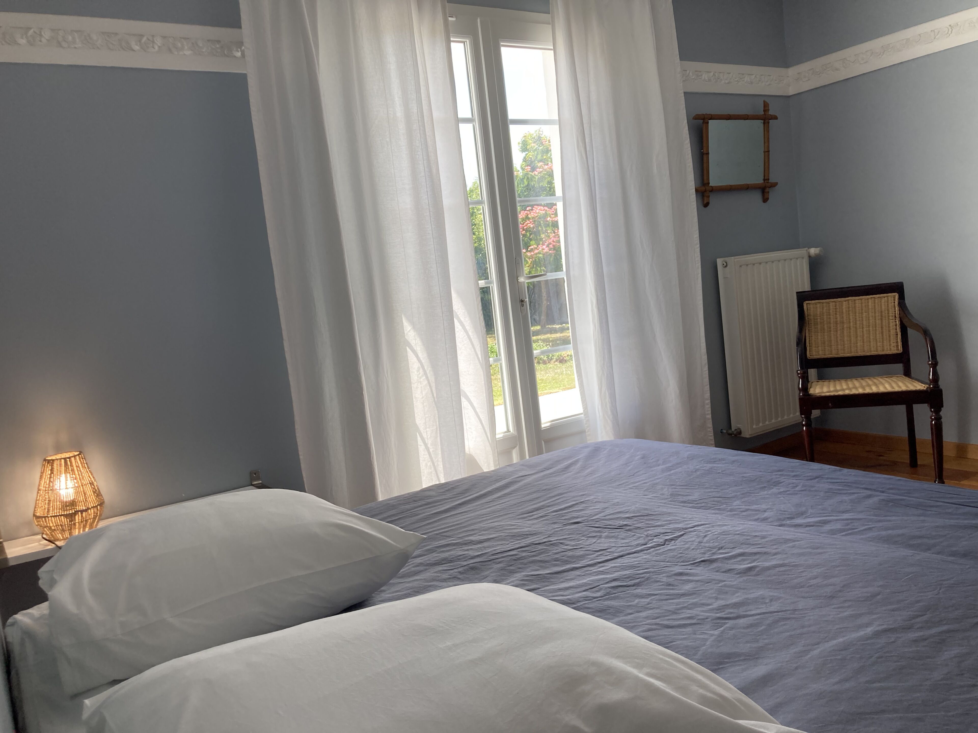 A bedroom with a bed, a chair, a lamp, and a window with curtains.