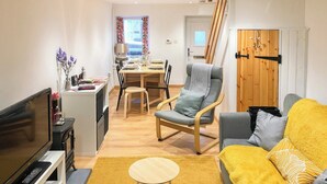 A modern living room with a TV, sofa, and a dining area with a table and chairs. - 2 bedroom accommodation in Amlwch (Amlwch)