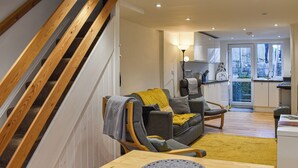 A modern apartment with a wooden staircase, a grey sofa with a yellow throw, a wooden dining table, and a view of the city through large windows. - 2 bedroom accommodation in Amlwch (Amlwch)