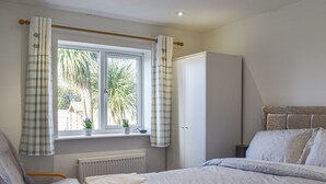 A bedroom with a bed, a chair, a radiator, and a window with curtains. - 2 bedroom accommodation in Amlwch (Amlwch)
