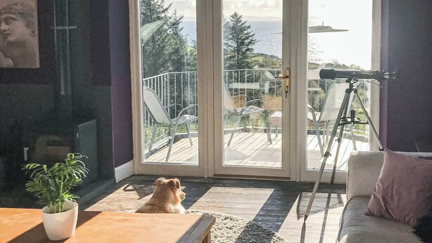 A room with a large sliding glass door leading to a balcony with a telescope.