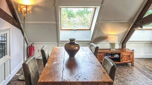 A wooden dining table with chairs, a vase, and a lamp in a room with a sloped ceiling and a window.