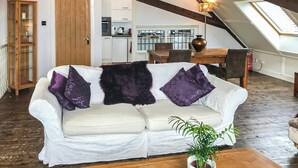 A loft-style room with a white sofa, a wooden dining table, and a kitchen in the background.