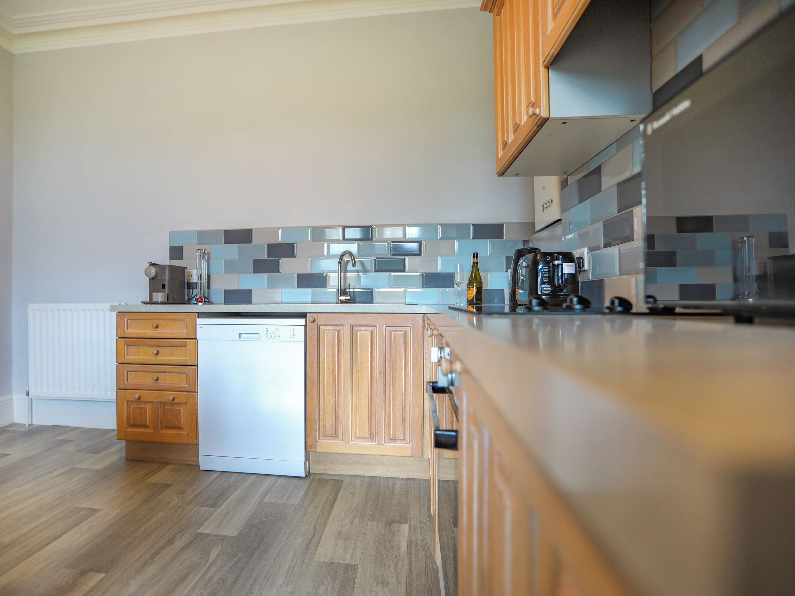 A modern kitchen with wooden cabinets, a dishwasher, a coffee maker, and a tiled backsplash.