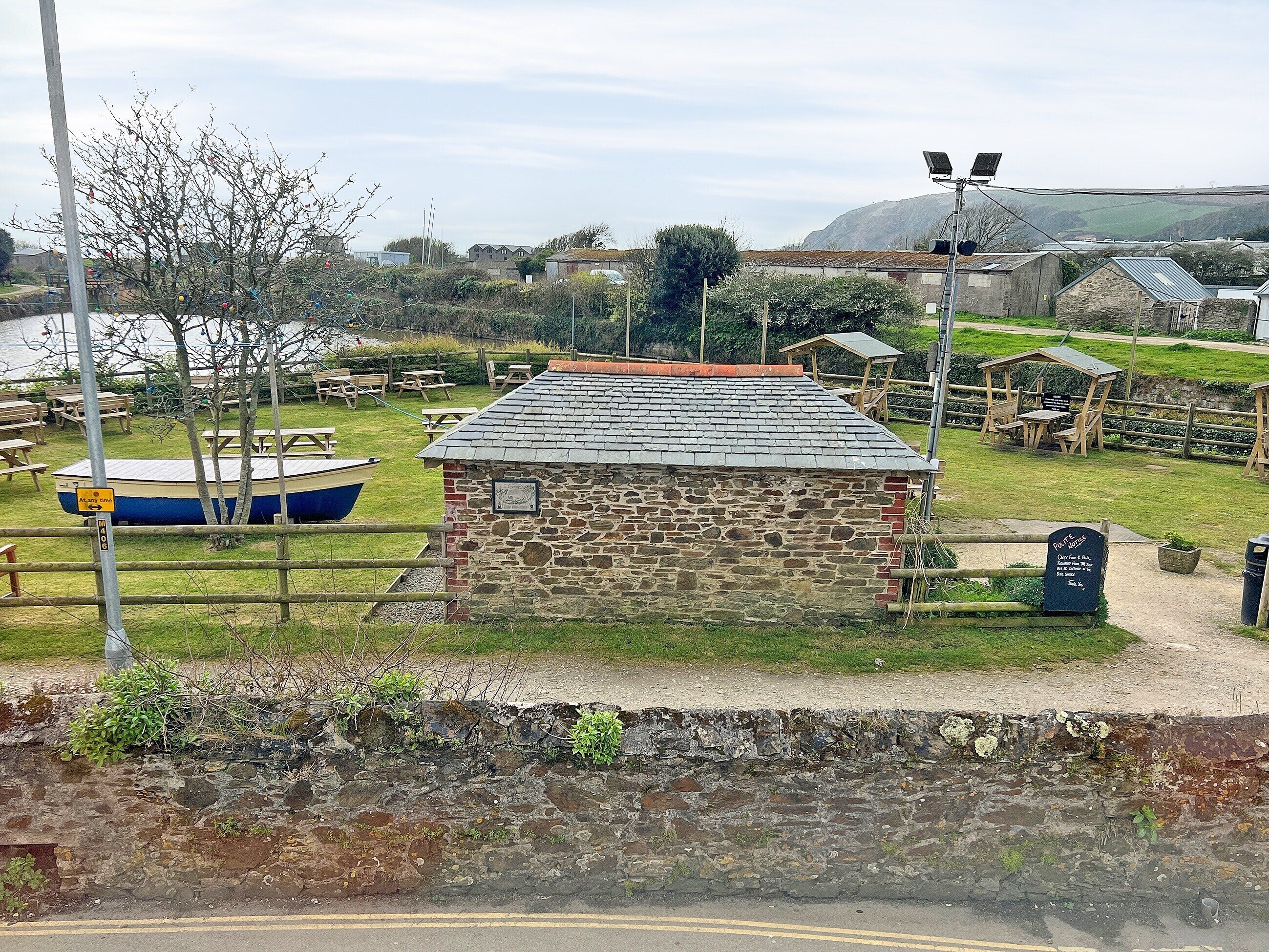A stone building with a tiled roof, surrounded by picnic tables and a boat.