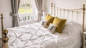 A neatly made bed with a white duvet, gold pillows, and a view of a garden through a window. - 1 bedroom accommodation in Mevagissey (Mevagissey)