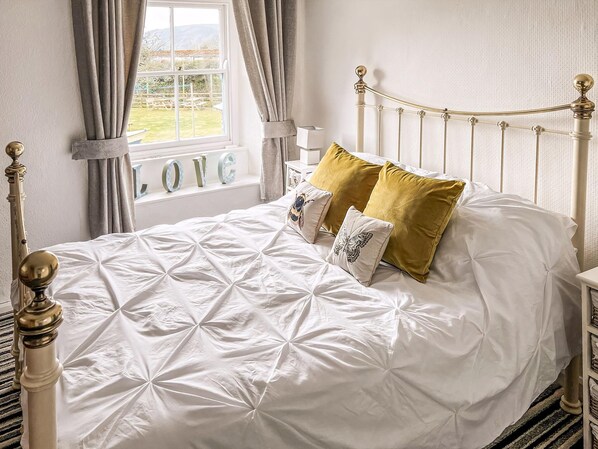 A neatly made bed with a white duvet, gold pillows, and a view of a garden through a window.