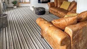 A living room with striped carpet, leather sofas, a clock, a TV, and a bookshelf. - 1 bedroom accommodation in Mevagissey (Mevagissey)