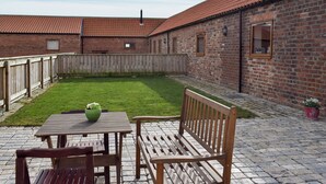 A courtyard with a brick building, a wooden fence, a table with chairs, and a green bowl. - 2 bedroom accommodation in Easby Grange, near Great Ayton (Easby Grange, near Great Ayton)