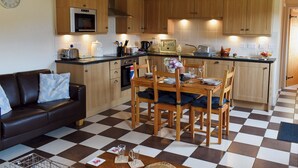 A compact kitchen with wooden cabinets, a dining table set for four, and a checkered floor. - 2 bedroom accommodation in Easby Grange, near Great Ayton (Easby Grange, near Great Ayton)