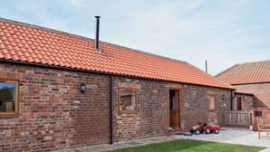 A brick building with a red-tiled roof, a wooden door, and a small lawn area with a red toy car. - 2 bedroom accommodation in Easby Grange, near Great Ayton (Easby Grange, near Great Ayton)