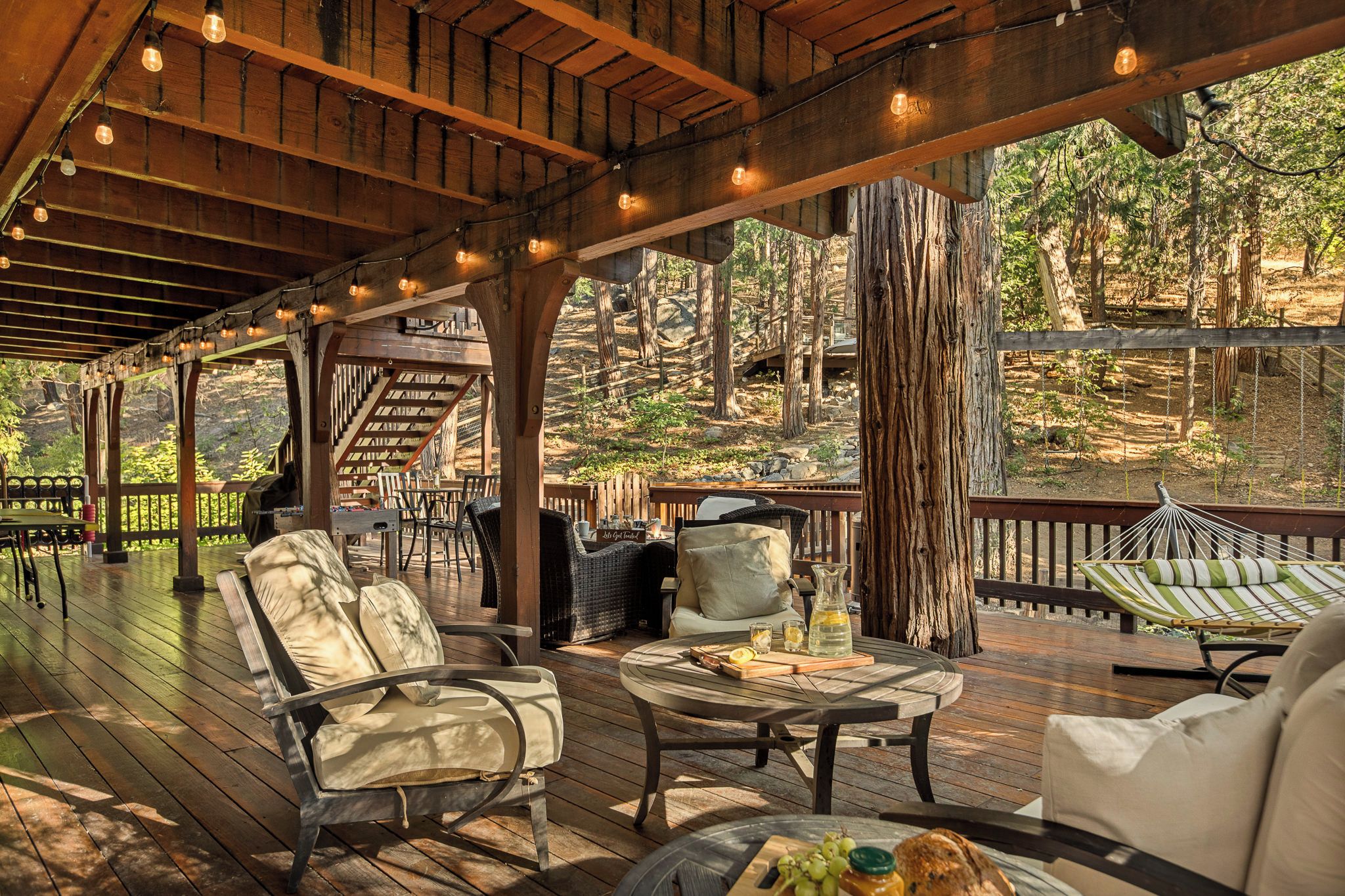 An outdoor patio with wooden furniture, a table with a bottle and glasses, and a hammock.