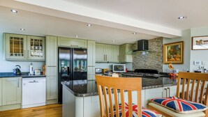 A modern kitchen with a central island, wooden chairs with Union Jack cushions, and a stainless steel refrigerator. - 5 bedroom accommodation in Ludham (Ludham)