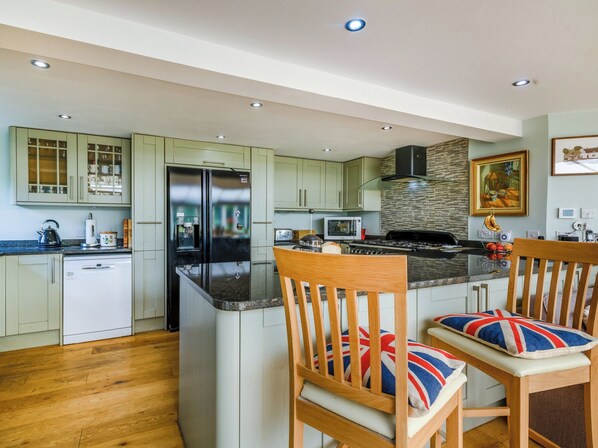 A modern kitchen with a central island, wooden chairs with Union Jack cushions, and a stainless steel refrigerator. - 5 bedroom accommodation in Ludham (Ludham)