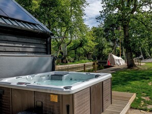 Un jacuzzi con una terraza de madera y un edificio de madera al fondo.
