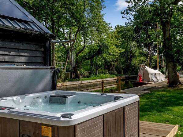 Un jacuzzi en un área boscosa con una terraza de madera y una zona cubierta al fondo.