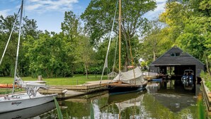 A marina with boats docked, a wooden boathouse, and a grassy area with trees. - 5 bedroom accommodation in Ludham (Ludham)