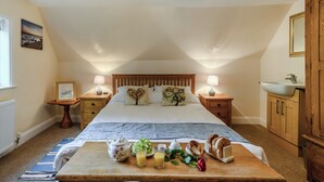 A bedroom with a large bed, bedside tables with lamps, a wooden headboard, a wooden cabinet, and a breakfast tray with fruits and a teapot. - 5 bedroom accommodation in Ludham (Ludham)