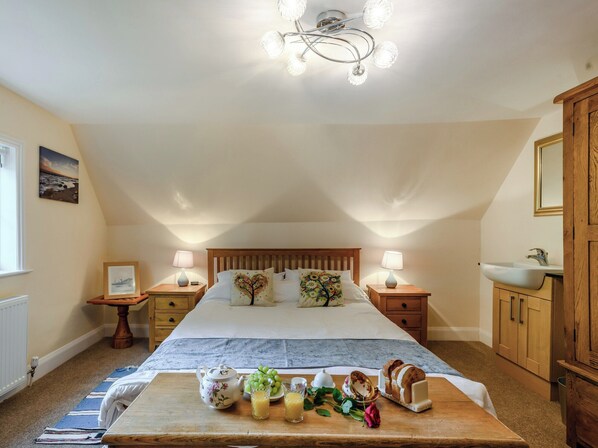 Une chambre avec un grand lit, des tables de chevet avec des lampes, une tête de lit en bois, une commode en bois et un plateau de petit-déjeuner avec des fruits et une théière.