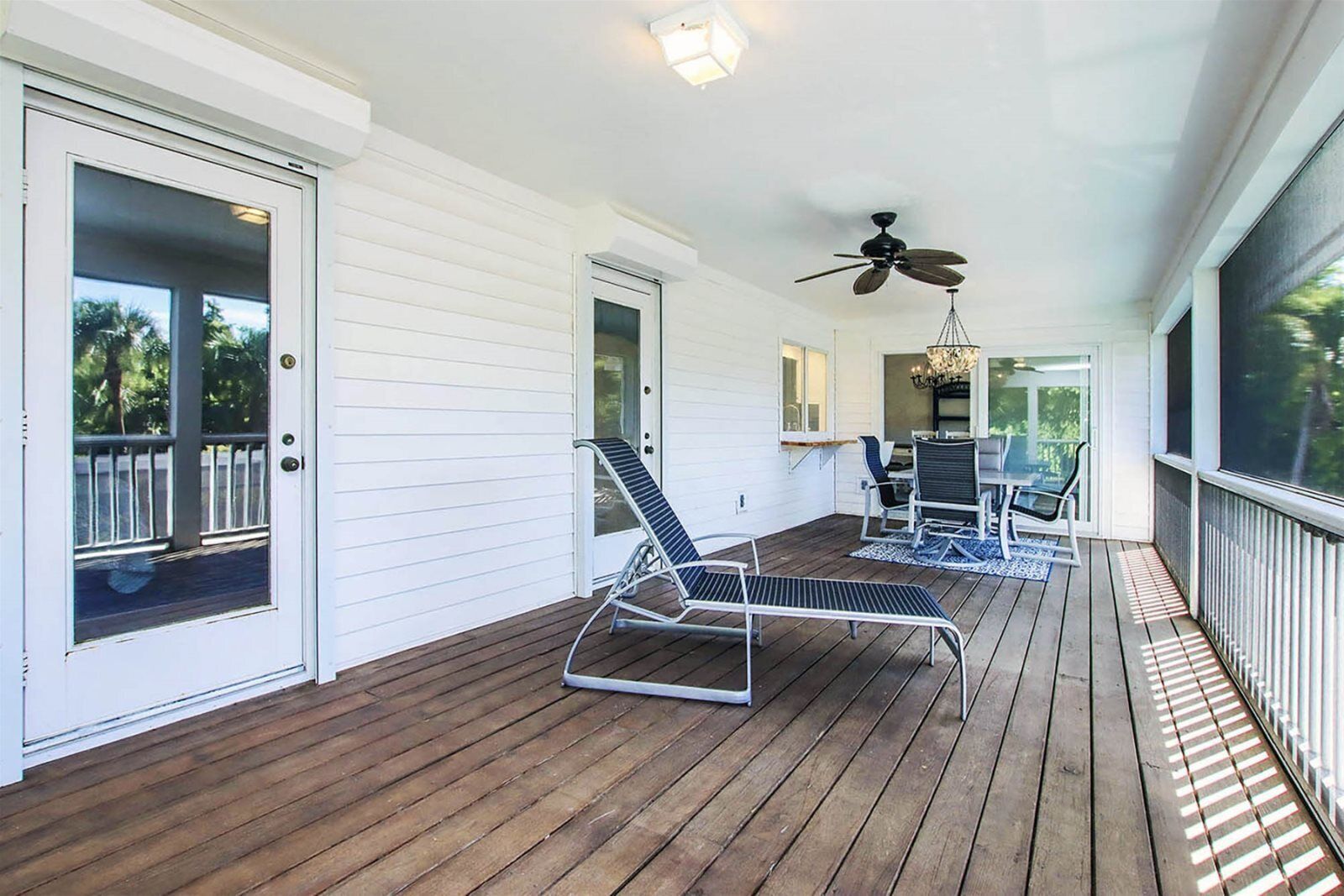 A covered porch with wooden flooring, a ceiling fan, and two chairs.
