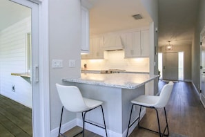 A kitchen with white cabinets, a granite countertop, and two white bar stools. - My Sand Castle (Sanibel)