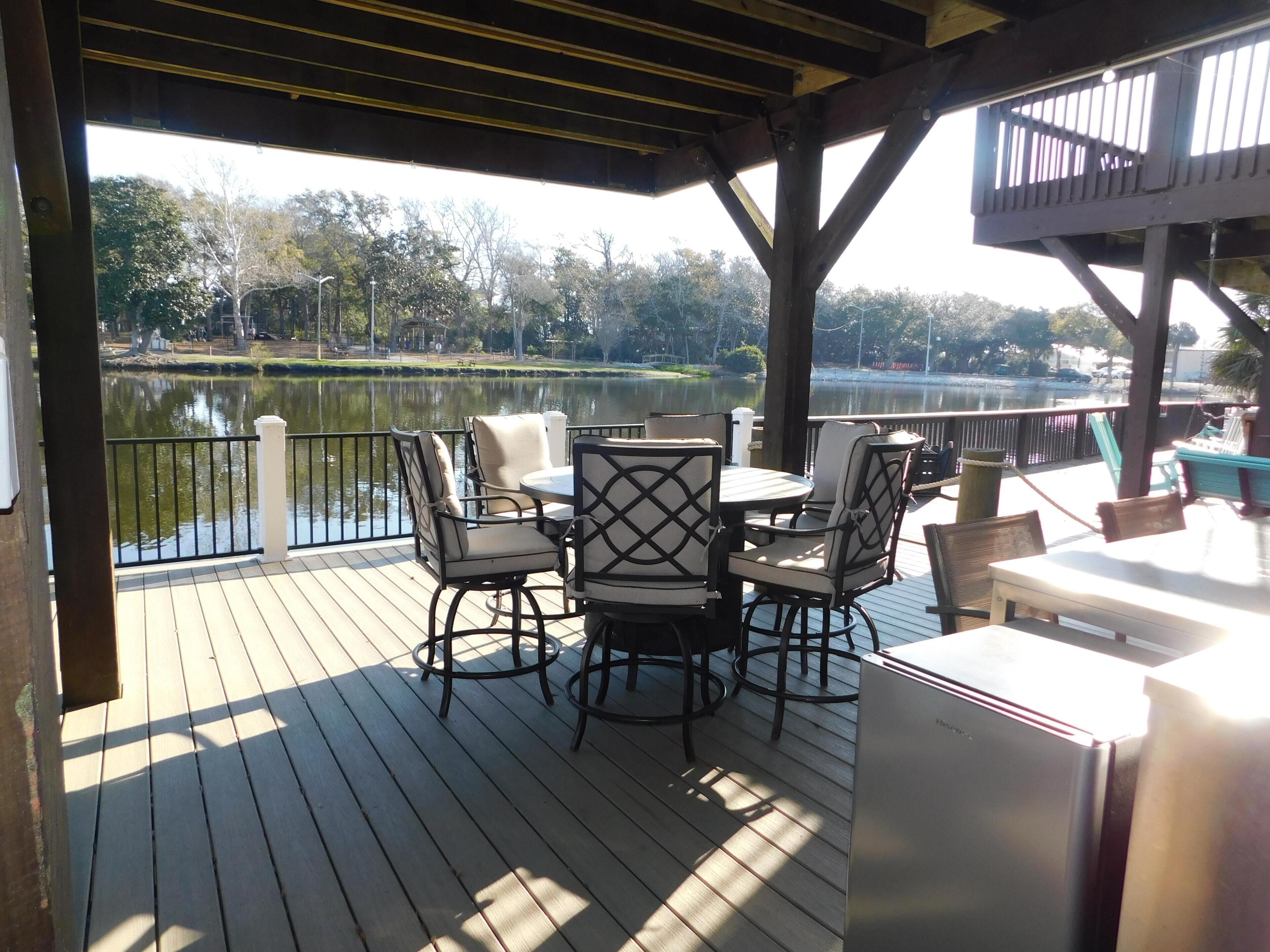 A covered outdoor deck with a table and chairs, overlooking a calm lake and park.