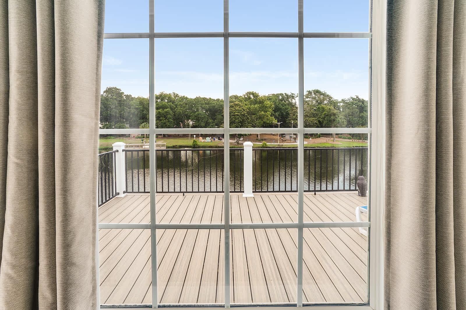 Un balcon donnant sur un lac, une terrasse en bois et une rambarde en métal.