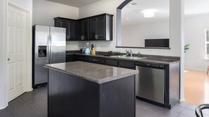 A modern kitchen with dark cabinets, a granite countertop island, stainless steel appliances, and a large window. - Modern South Austin Home|King Bed • Gym • Patio • Sleeps 6- Ideal for long stays (Austin)