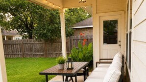 A covered patio with a table and two sofas, a string of lights, and a wooden fence in the background. - Modern South Austin Home|King Bed • Gym • Patio • Sleeps 6- Ideal for long stays (Austin)