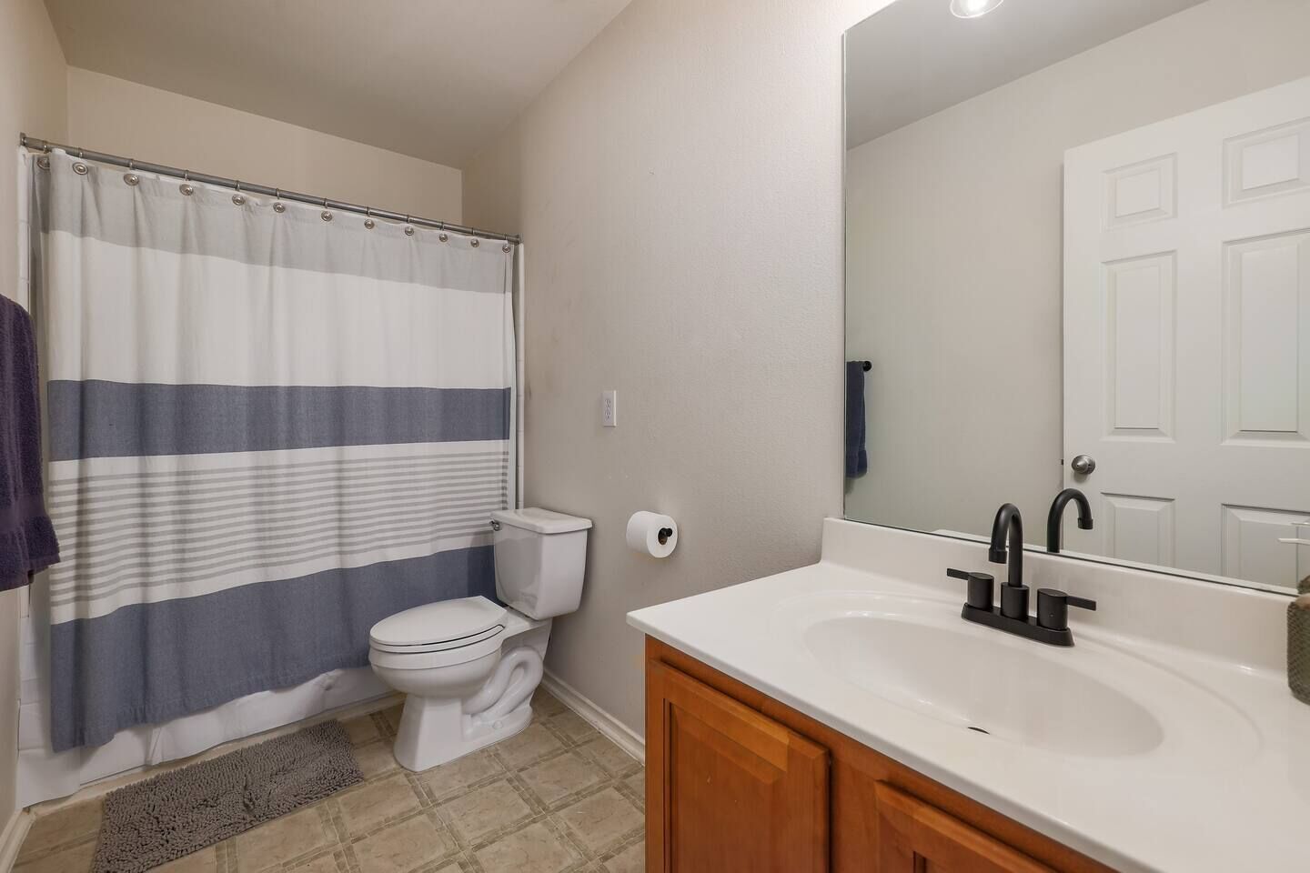 Une salle de bain avec un rideau de douche à rayures, des toilettes, un lavabo avec un miroir et des meubles en bois.