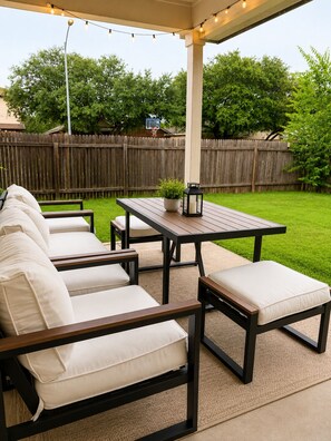 An outdoor patio with a wooden table, two cushioned chairs, a small potted plant, and a lantern. - Modern South Austin Home|King Bed • Gym • Patio • Sleeps 6- Ideal for long stays (Austin)