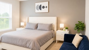 A bedroom with a bed, a nightstand, a desk, a chair, a ceiling fan, a window, and a wall-mounted artwork. - Modern South Austin Home|King Bed • Gym • Patio • Sleeps 6- Ideal for long stays (Austin)
