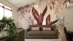 Un salon avec un canapé, un luminaire suspendu et un mur orné d’une fresque florale.